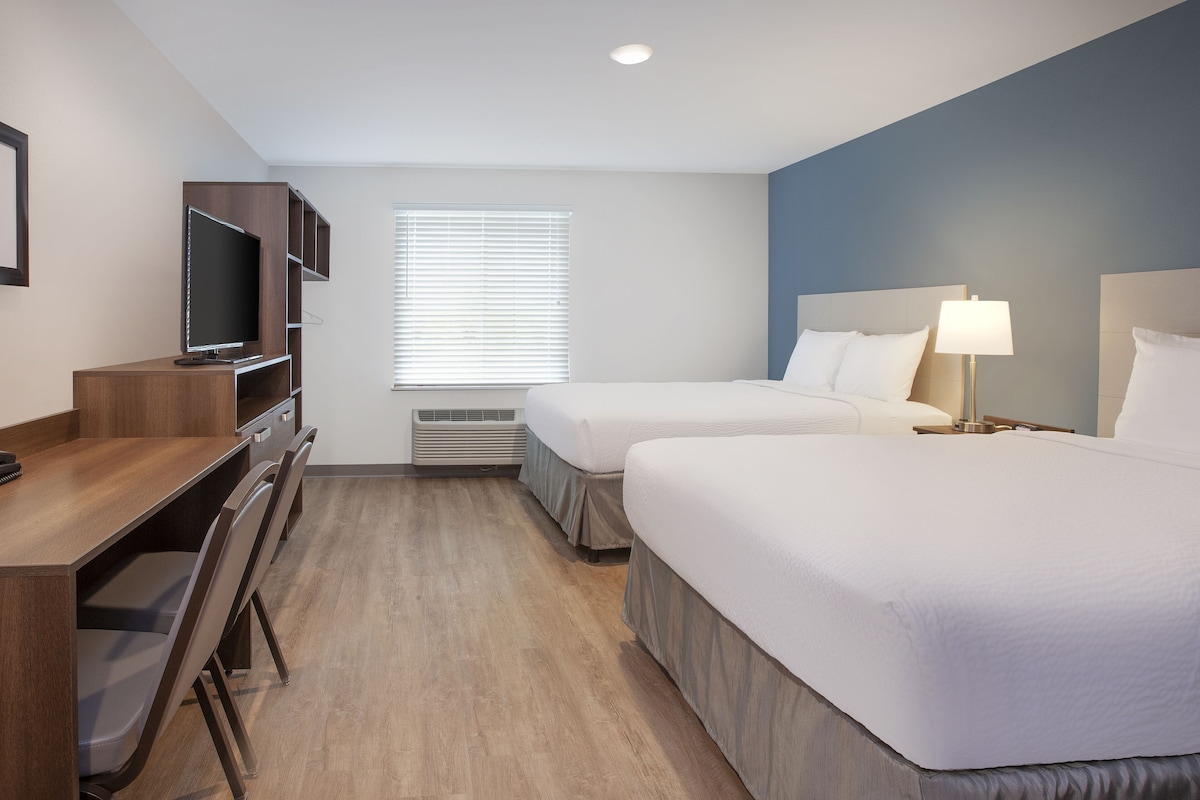 A hotel room with two beds, a desk with a chair, a television, and a window with blinds.