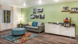 Una sala moderna con un sofá gris, un reposapiés azul y un mueble blanco con una cafetera.