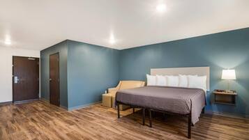 A hotel room with a bed, a chair, a bedside table with a lamp, and a door.
