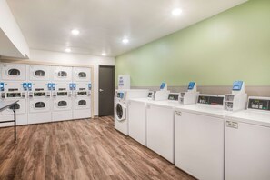 A laundry facility with multiple washing machines and dryers, a soap dispenser, and a digital control panel. - WoodSpring Suites Atlanta Newnan (Newnan)