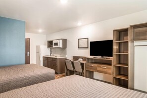 A hotel room with two beds, a kitchenette, a desk with a chair, a television, and a wardrobe. - WoodSpring Suites Atlanta Newnan (Newnan)