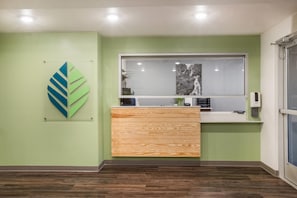 A reception area with a wooden counter, a framed abstract artwork, and a window with a waterfall view. - WoodSpring Suites Atlanta Newnan (Newnan)