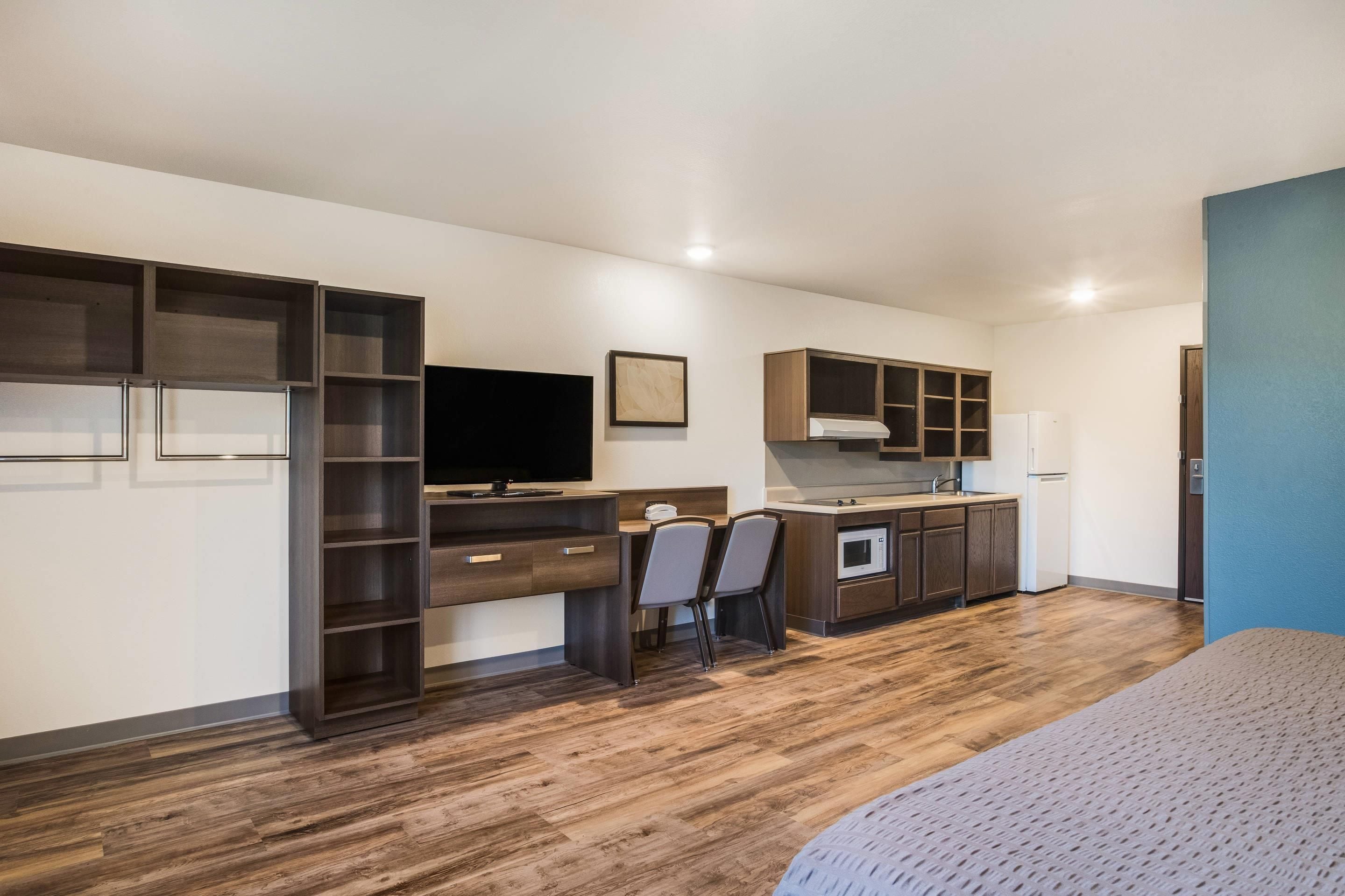 Habitación compacta con cama, escritorio, silla, televisor y kitchenette.