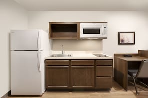 A compact kitchen with a white refrigerator, a microwave, and wooden cabinets. - WoodSpring Suites Atlanta Newnan (Newnan)