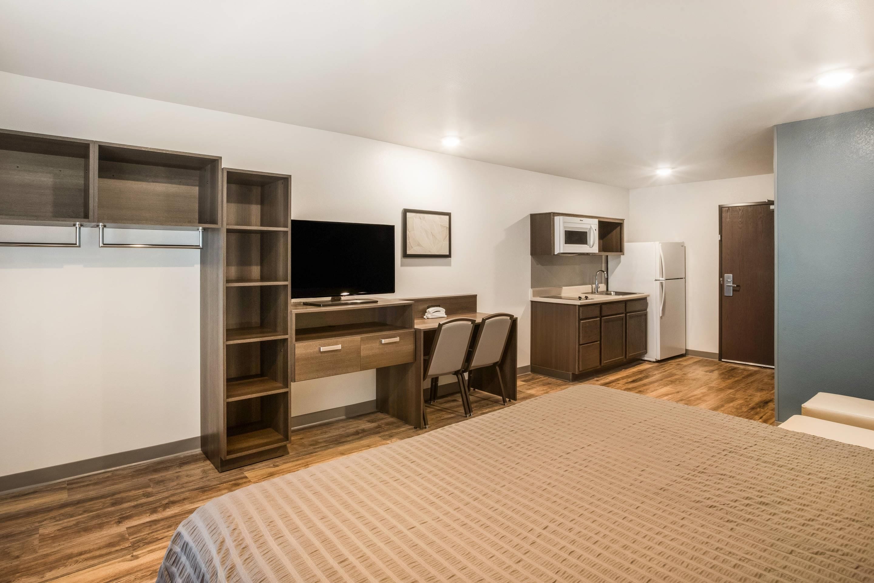 A compact room with a bed, a desk, a chair, a television, a microwave, and a refrigerator.