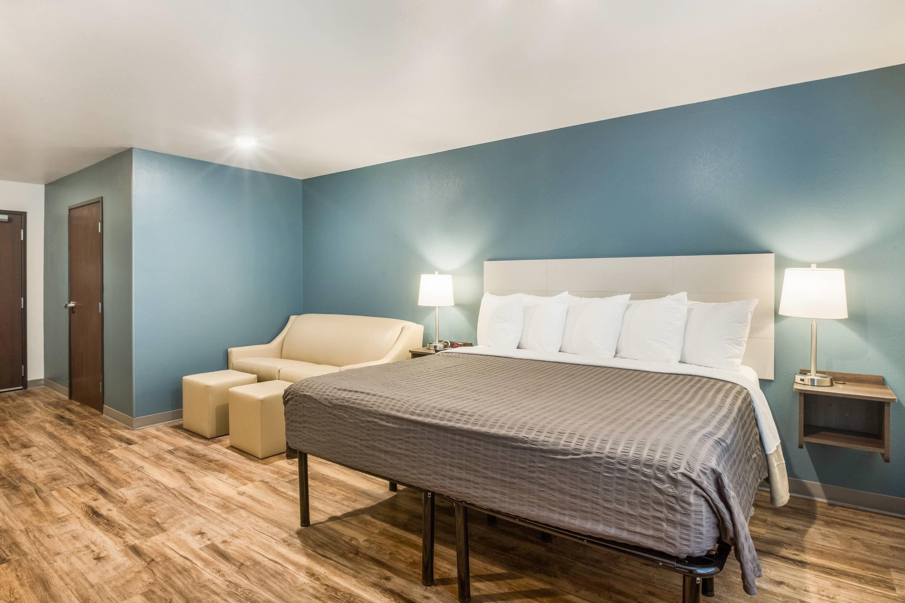 Una habitación de hotel con una cama, una silla, una mesita de noche y una lámpara.