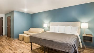 Una habitación de hotel con una cama, una silla, una mesita de noche y una lámpara.
