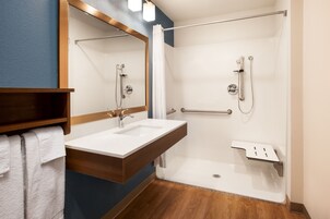Un baño moderno con tocador de madera, un lavamanos blanco y cabina de ducha de cristal.