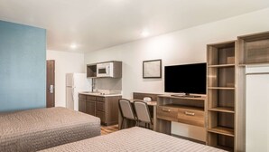 Habitación de hotel con dos camas, kitchenette, escritorio con silla, televisor y estantes empotrados.