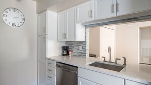A modern kitchen with white cabinets, a stainless steel dishwasher, a double sink, and a clock on the wall. - Pearl of Scottsdale Old Town Getaway 1BR (Scottsdale)