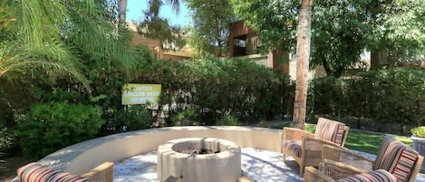Relax in a serene garden setting with a fire pit and wicker chairs.