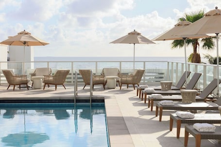 Una piscina al aire libre, sombrillas, sillones reclinables de piscina
