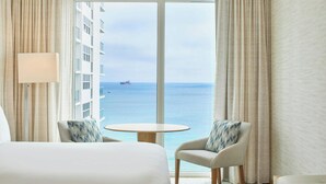 A hotel room with a bed, two armchairs, a small table, and a view of the ocean and a distant ship. - AC Hotel by Marriott Fort Lauderdale Beach (Fort Lauderdale)