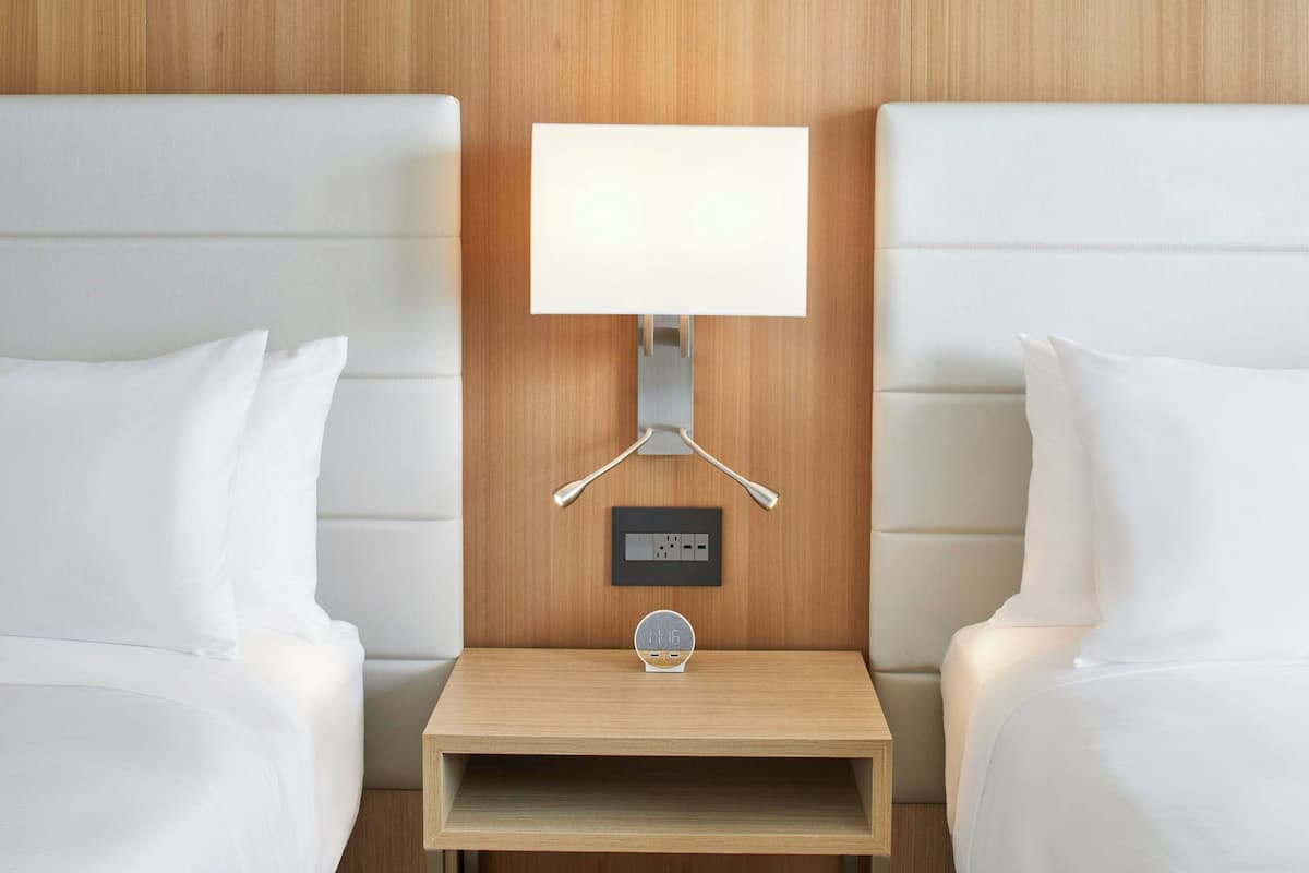Una habitación de hotel con dos camas, una mesita de noche con l ámpara y un enchufe.