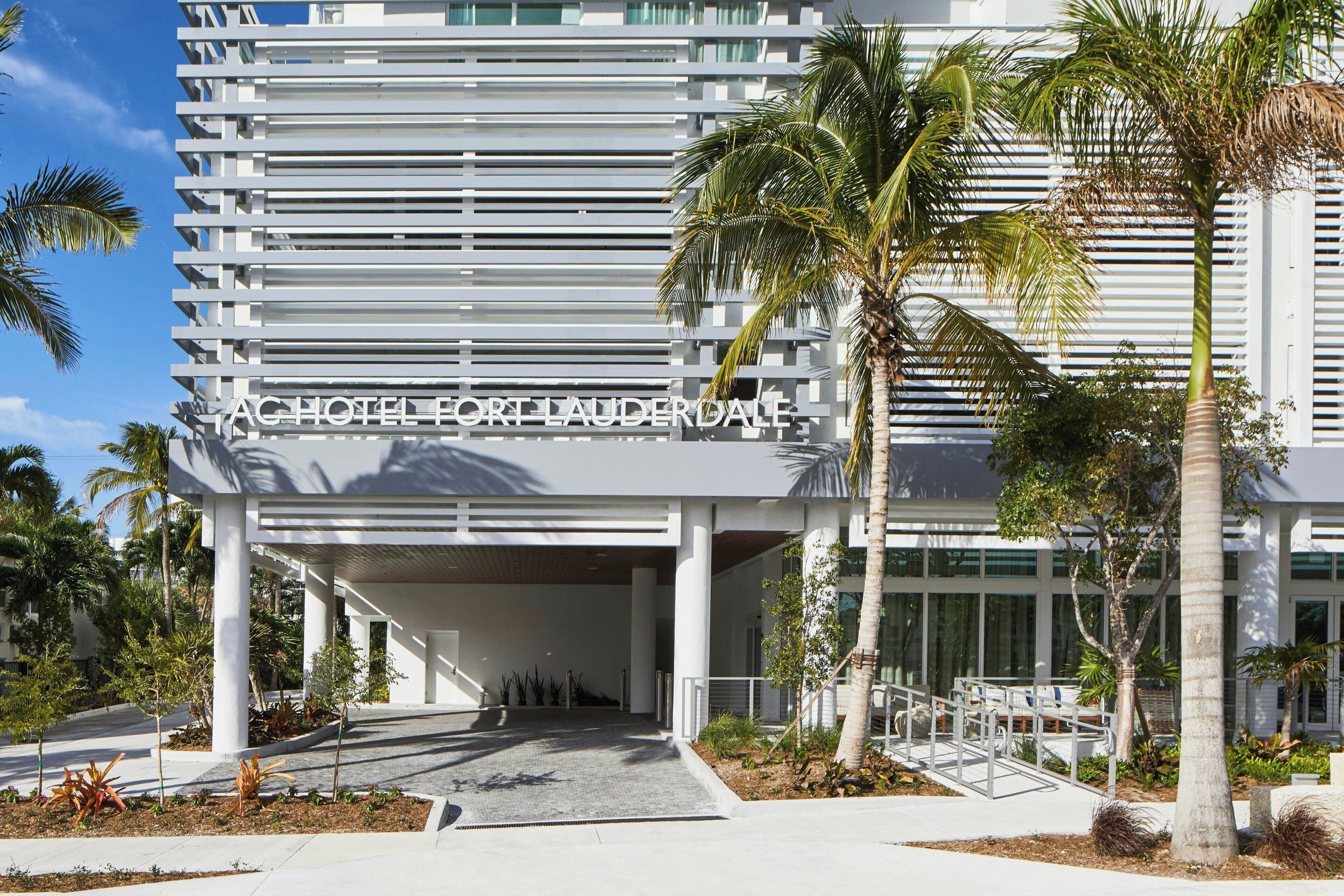 A modern hotel entrance with a horizontal facade, palm trees, and a clear sky.
