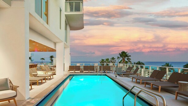 A pool area with lounge chairs and a view of the ocean at sunset. - AC Hotel by Marriott Fort Lauderdale Beach (Fort Lauderdale)
