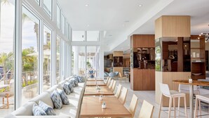 A modern dining area with long tables and benches, large windows, and a view of the outdoors. - AC Hotel by Marriott Fort Lauderdale Beach (Fort Lauderdale)