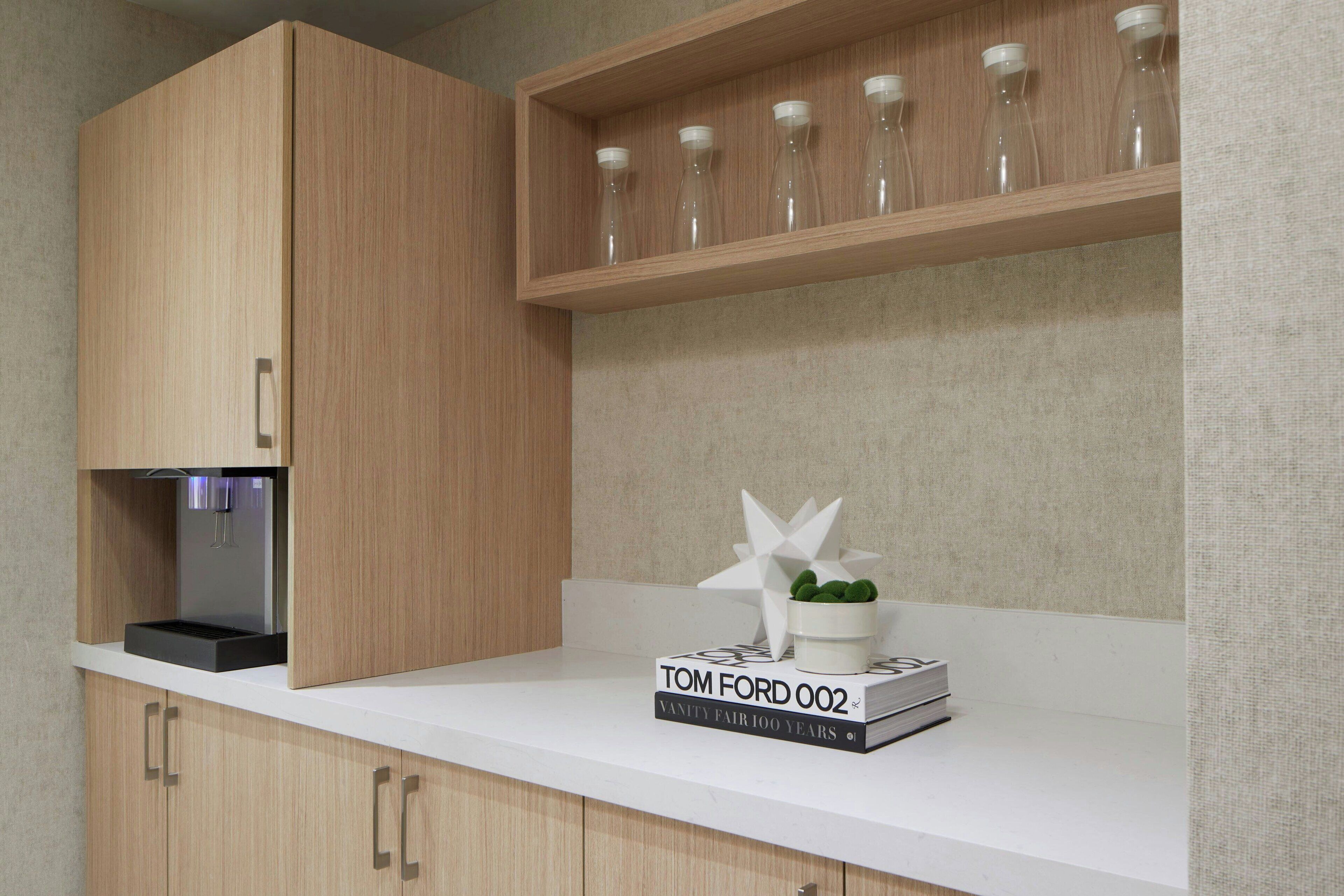 Una cucina moderna con mobili in legno, un piano di lavoro bianco e uno scaffale con bottiglie di vetro.