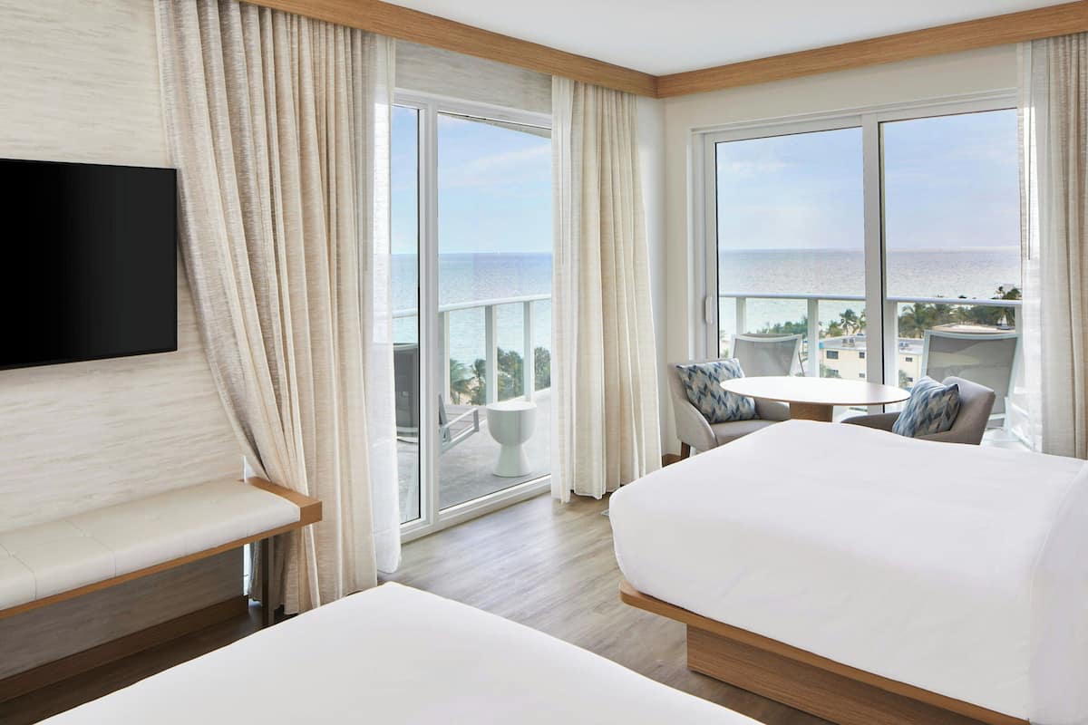 Habitación de hotel con cama, zona de estar, televisión y balcón con vistas al mar.