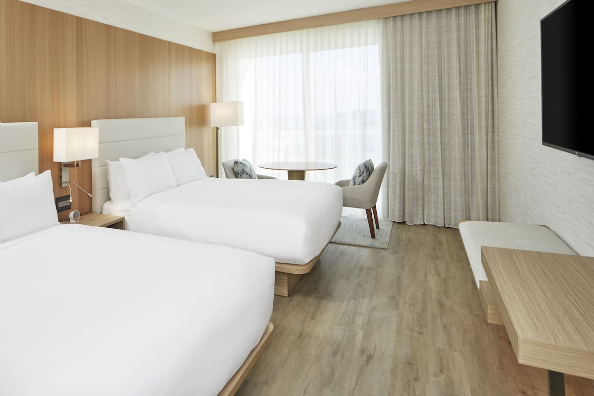 Habitación de hotel con dos camas, una mesita, una silla y un televisor.