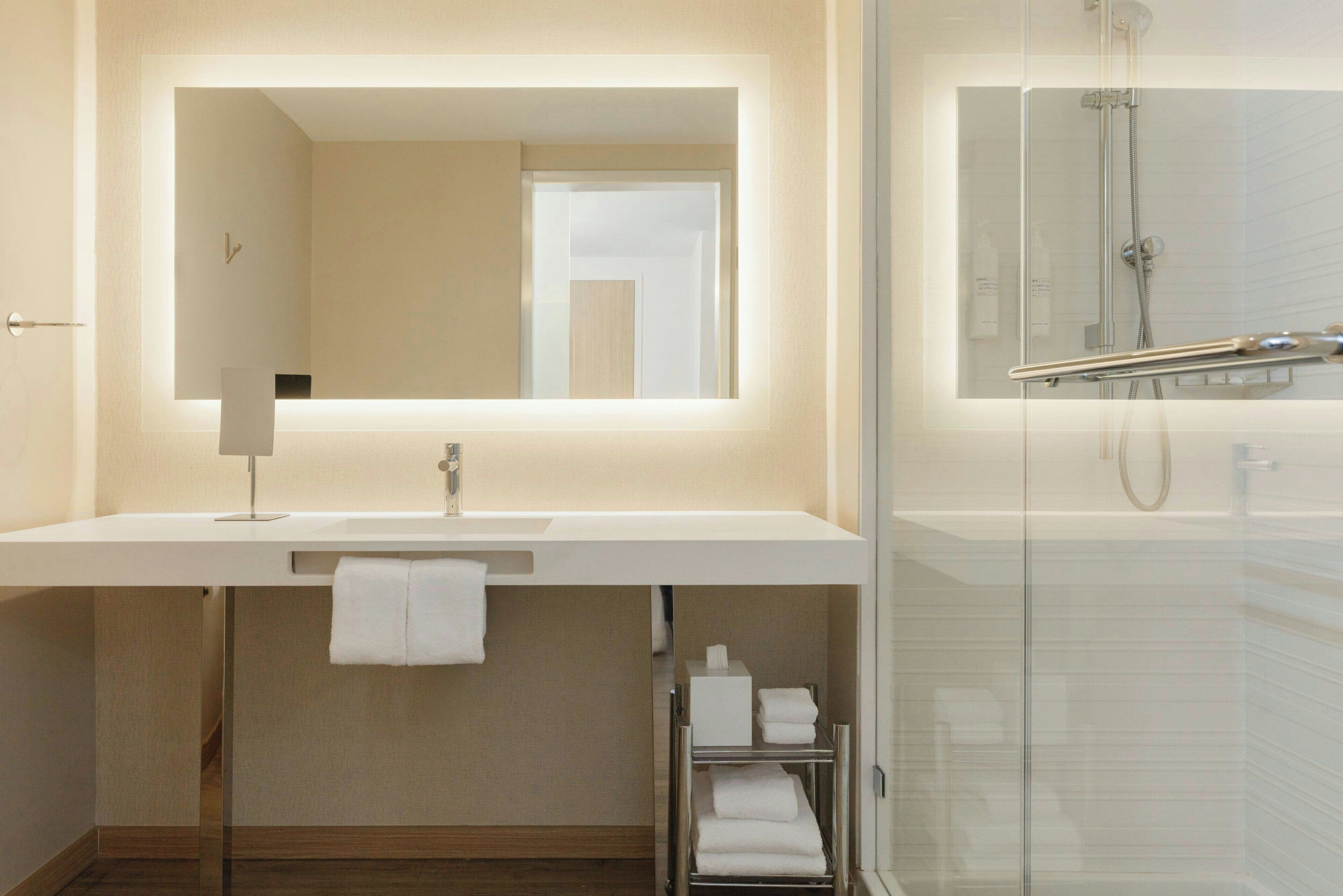 A modern bathroom with a large mirror, a white sink, and a glass-enclosed shower.
