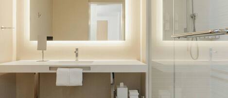 A modern bathroom with a large mirror, a white sink, and a glass-enclosed shower.