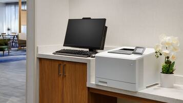 Un escritorio moderno con una computadora de escritorio, una impresora y una orquídea en maceta.