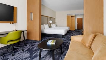 Una camera d'albergo con un letto, una poltrona verde, un tavolo nero e un divano color beige.