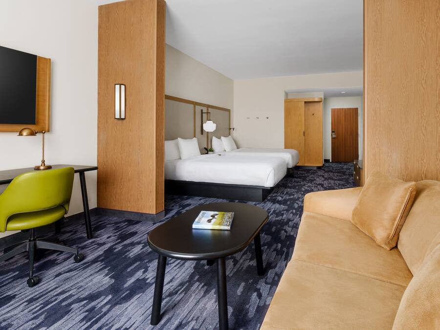 Een hotelkamer met een bed, een groene stoel, een zwarte tafel en een beigekleurde bank.