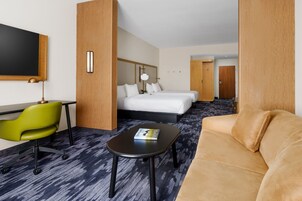 Una habitación de hotel con una cama, una silla verde, una mesa negra y un sofá beige.