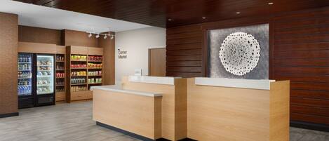 A reception area with a wooden reception desk, a refrigerator stocked with beverages, and a wall-mounted decorative piece.