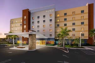 Un hotel de varios pisos con diseño moderno, que cuenta con una entrada destacada con área cubierta y un estacionamiento frente a él.