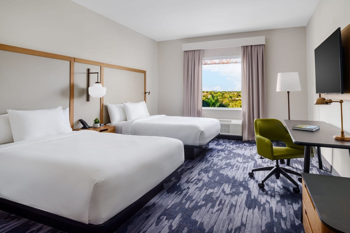 A hotel room with two beds, a desk, a chair, a TV, and a window with a view.