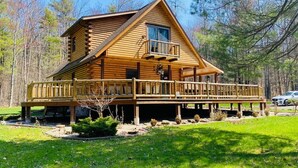 A log cabin with a balcony, surrounded by a grassy area and trees. - secluded log home, minutes from all star village in Oneonta (Laurens)