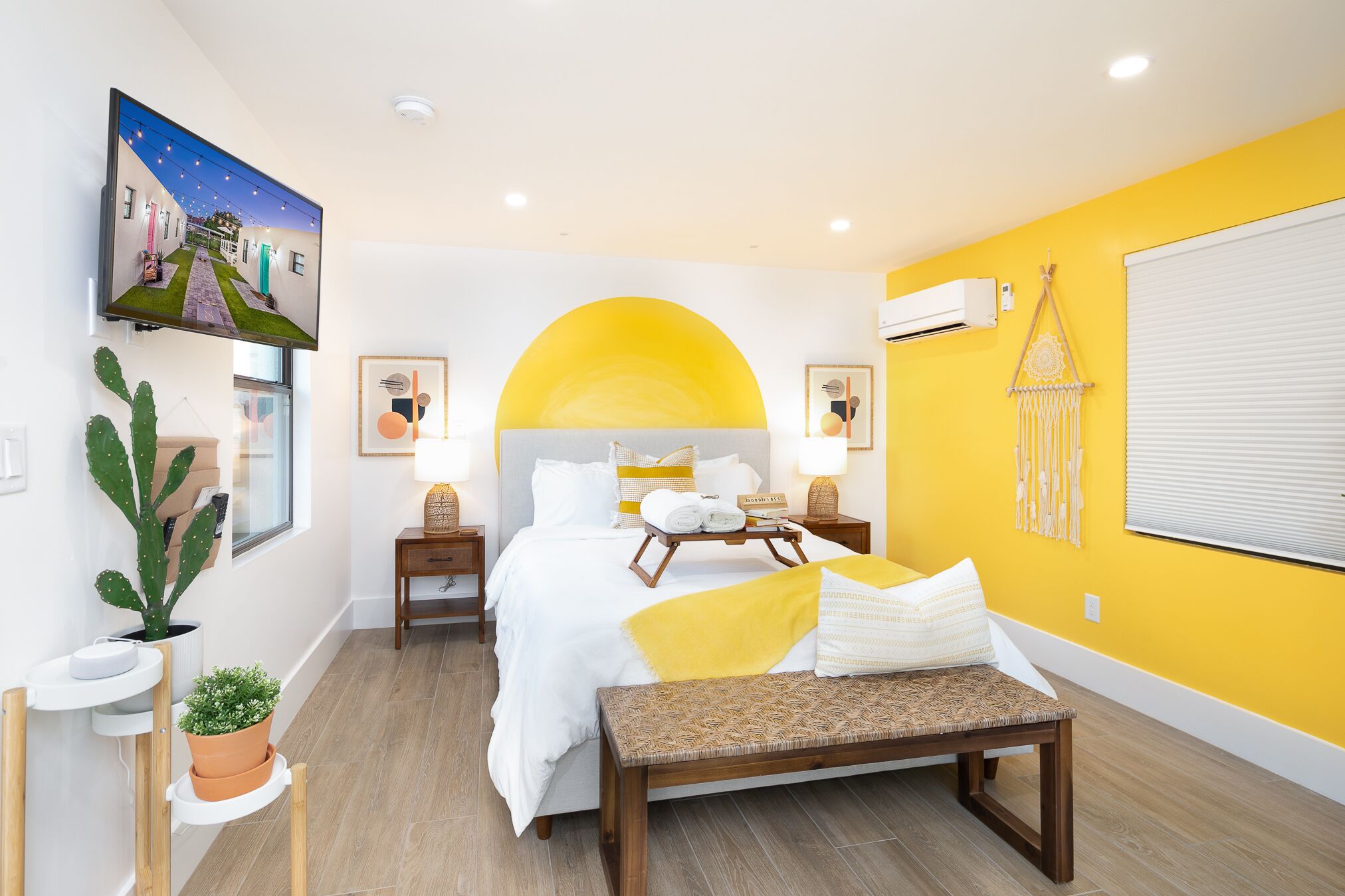 A modern hotel room with a bed, bedside tables, a bench, and a large window.