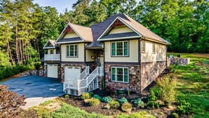 A two-story house with a stone foundation and a beige exterior, featuring a front porch and a driveway. - Luxury Villa! Backyard, 1 mile to Parkway! Hot tub & Gameroom!  (Sevierville)