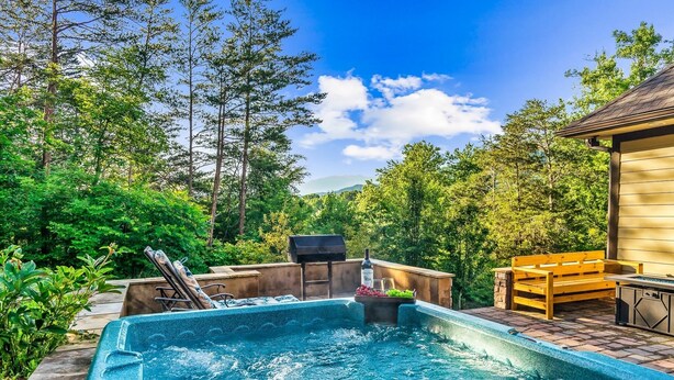 A hot tub surrounded by a wooden deck, with a barbecue grill and seating area. - Luxury Villa! Backyard, 1 mile to Parkway! Hot tub & Gameroom!  (Sevierville)