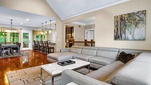 A spacious living room with a large grey sectional sofa, a marble coffee table, and a dining area with a table and chairs. - Luxury Villa! Backyard, 1 mile to Parkway! Hot tub & Gameroom!  (Sevierville)