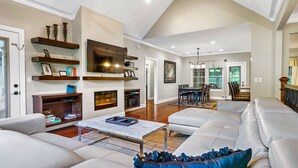 A spacious living room with a large sectional sofa, a flat-screen TV mounted on a wall, and built-in shelves with decorative items. - Luxury Villa! Backyard, 1 mile to Parkway! Hot tub & Gameroom!  (Sevierville)
