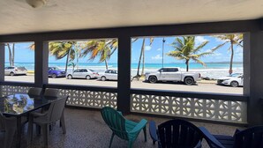 Un espace extérieur abrité, aménagé avec des sièges, d’où l’on peut admirer la plage et les voitures garées.