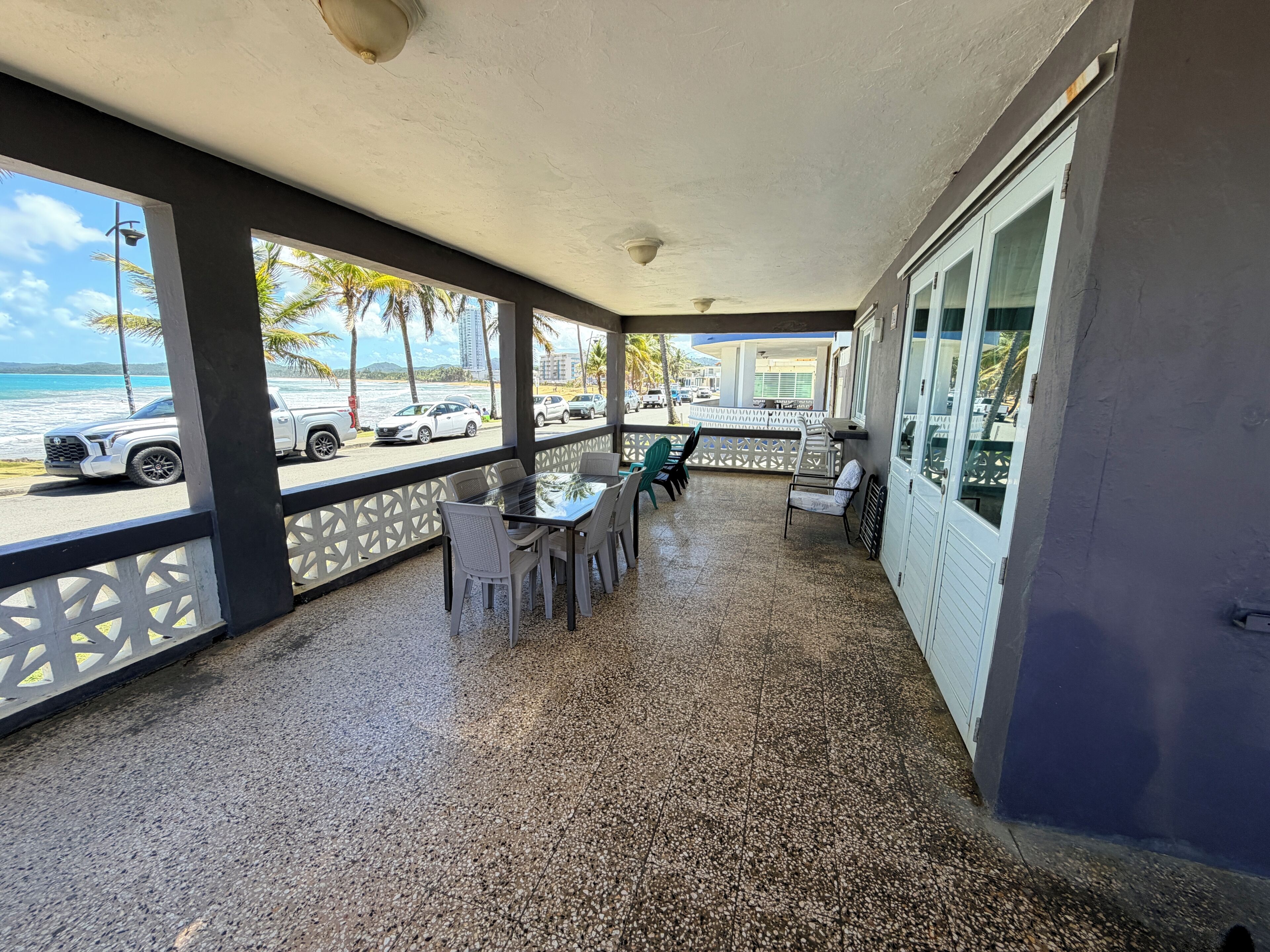 Un espace extérieur abrité, aménagé avec des sièges, d’où l’on peut admirer la plage et les voitures garées.