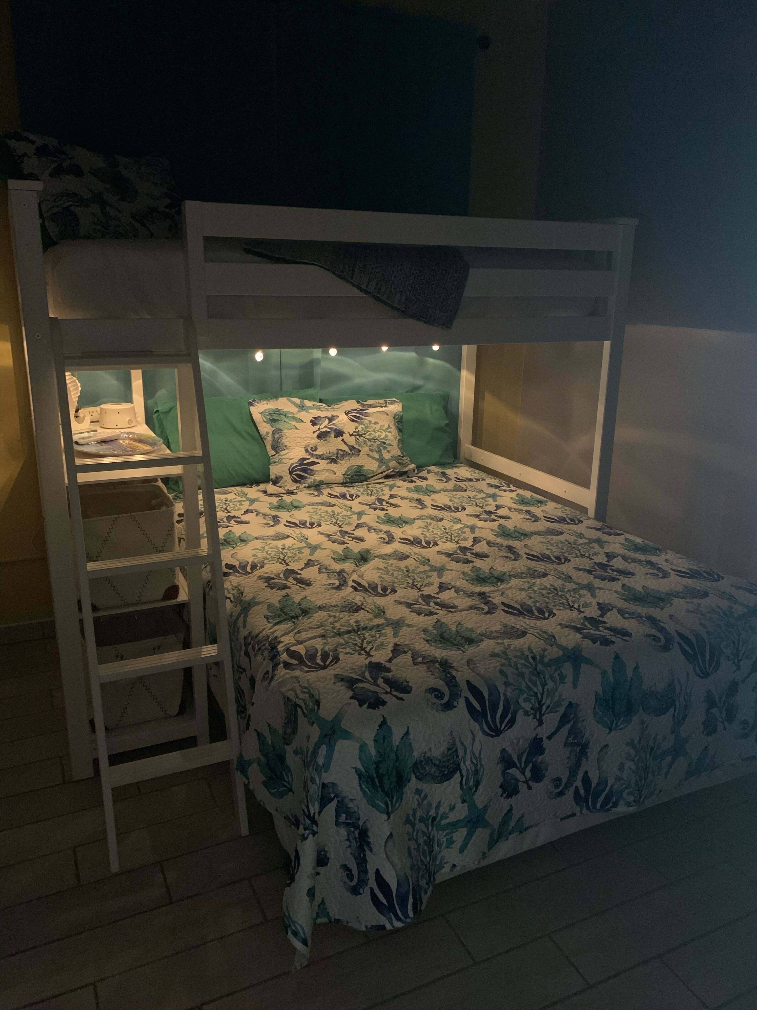A bunk bed with a ladder, a headboard with lights, and a floral bedspread.