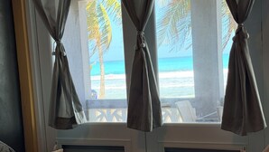 Une chambre avec vue sur la plage, un lit recouvert d’une couverture à motifs et une fenêtre dont les rideaux sont attachés.