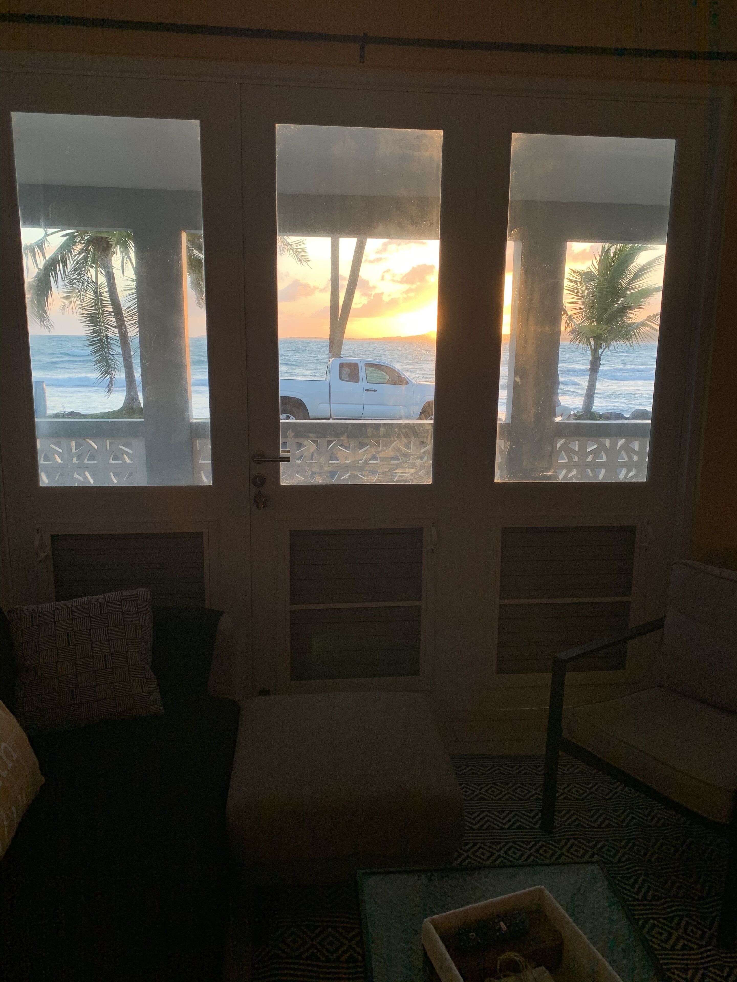 A room with a view of the ocean through a glass door, a white truck parked outside, and a patterned floor.