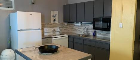 A modern kitchen with a white refrigerator, a stove, a sink, and a microwave. There are three pendant lights hanging above the counter.