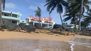 Une propriété située en bord de mer, avec un bâtiment moderne, de gros rochers et des palmiers.