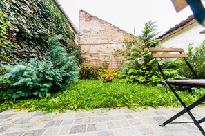A garden with a stone pathway, a wooden bench, and a brick wall. - Tischler Apartment & Studio (Sibiu)