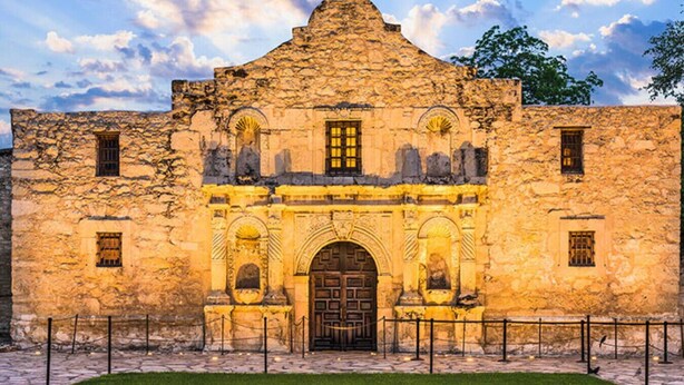 Ein historisches Steinhaus mit einem zentralen Rundbogenportal, das von kleineren Fenstern und dekorativen Elementen gesäumt wird.