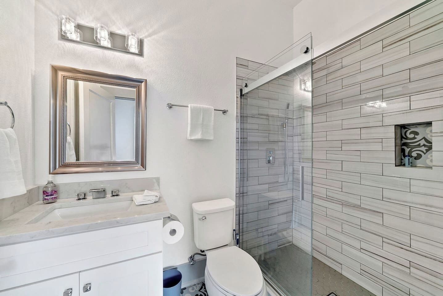 A modern bathroom with a glass shower enclosure, a large mirror, and a marble countertop.