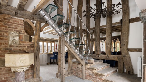 Un intérieur rustique avec des poutres apparentes, un escalier en colimaçon et une cheminée en pierre.